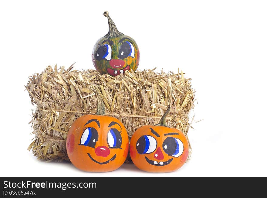 Small pumpkins with painted faces, and a bundle of hay, on white background. Small pumpkins with painted faces, and a bundle of hay, on white background.