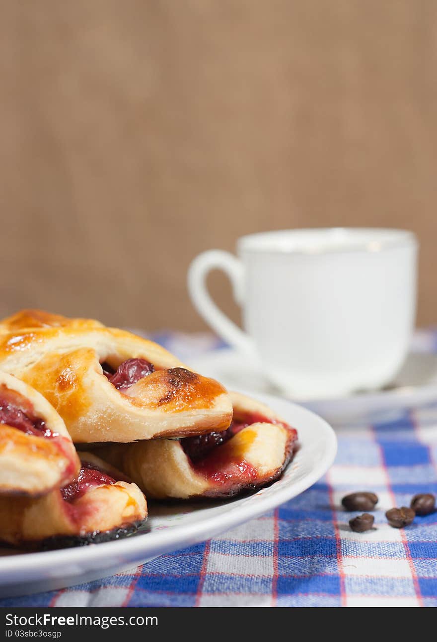 Cherry bun on a plate and cup of coffee