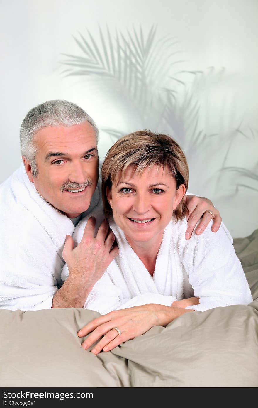 Mature couple in bathrobes on a bed. Mature couple in bathrobes on a bed