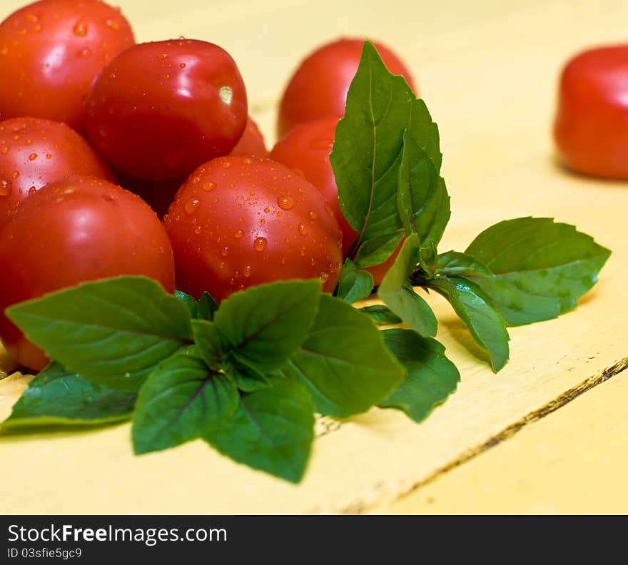 Pile of tomatos and basil leaves on wooden table