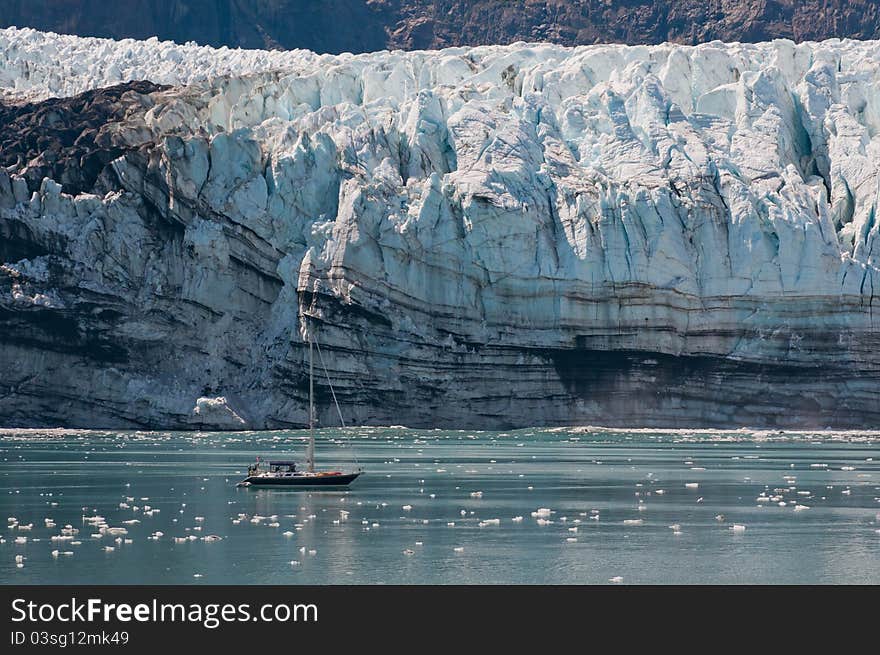 Tiny sailing boat with majestic glacier in background showing contrast. Tiny sailing boat with majestic glacier in background showing contrast.