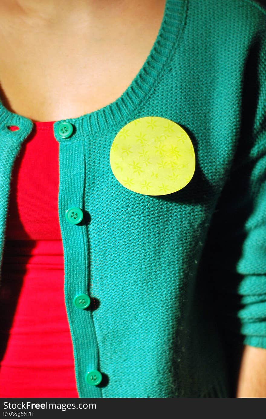 Close up of a blank yellow sticker on person wearing a green vest with a red t-shirt. Close up of a blank yellow sticker on person wearing a green vest with a red t-shirt