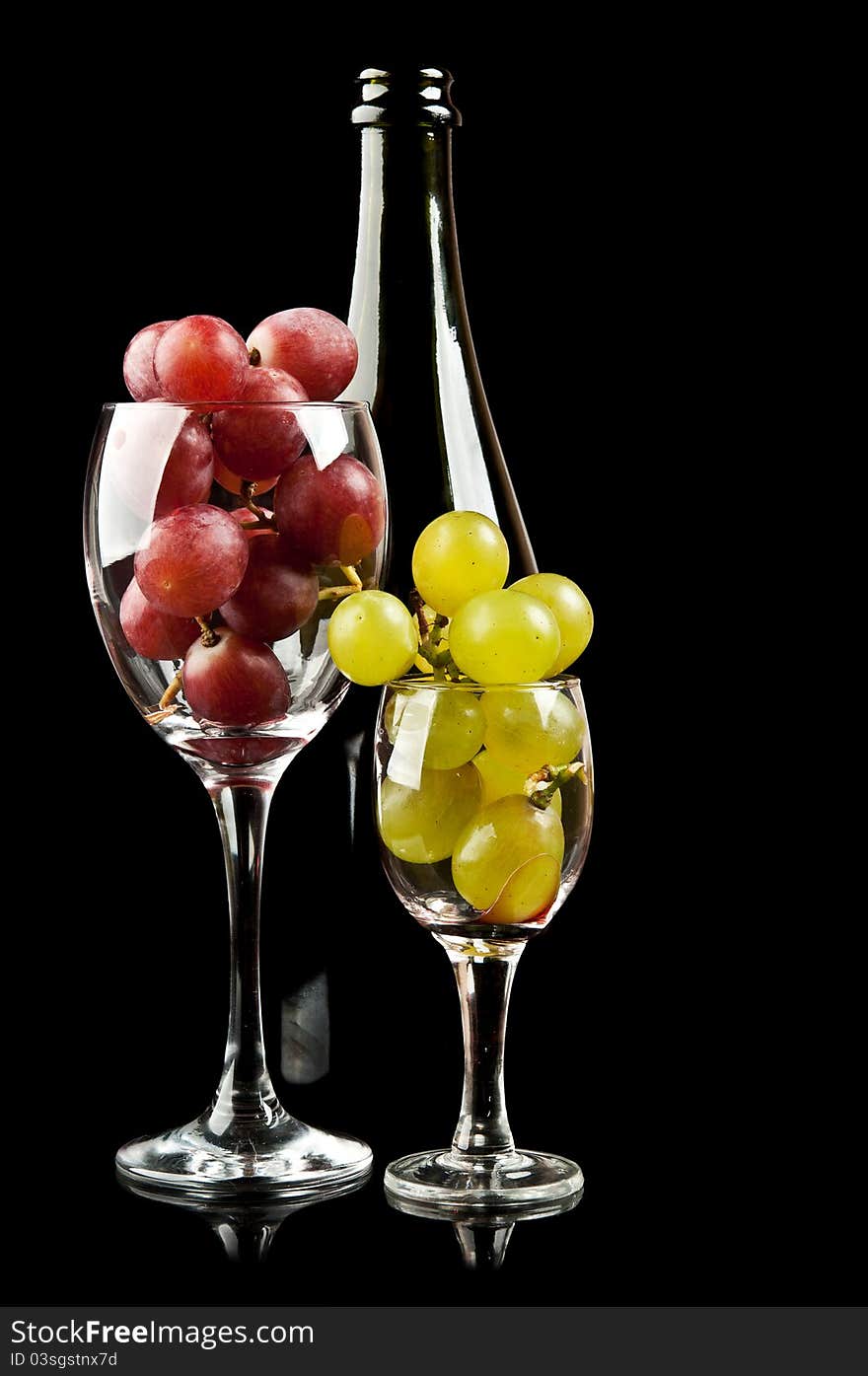 Grapes in a glass and a bottle of wine isolated on a black background