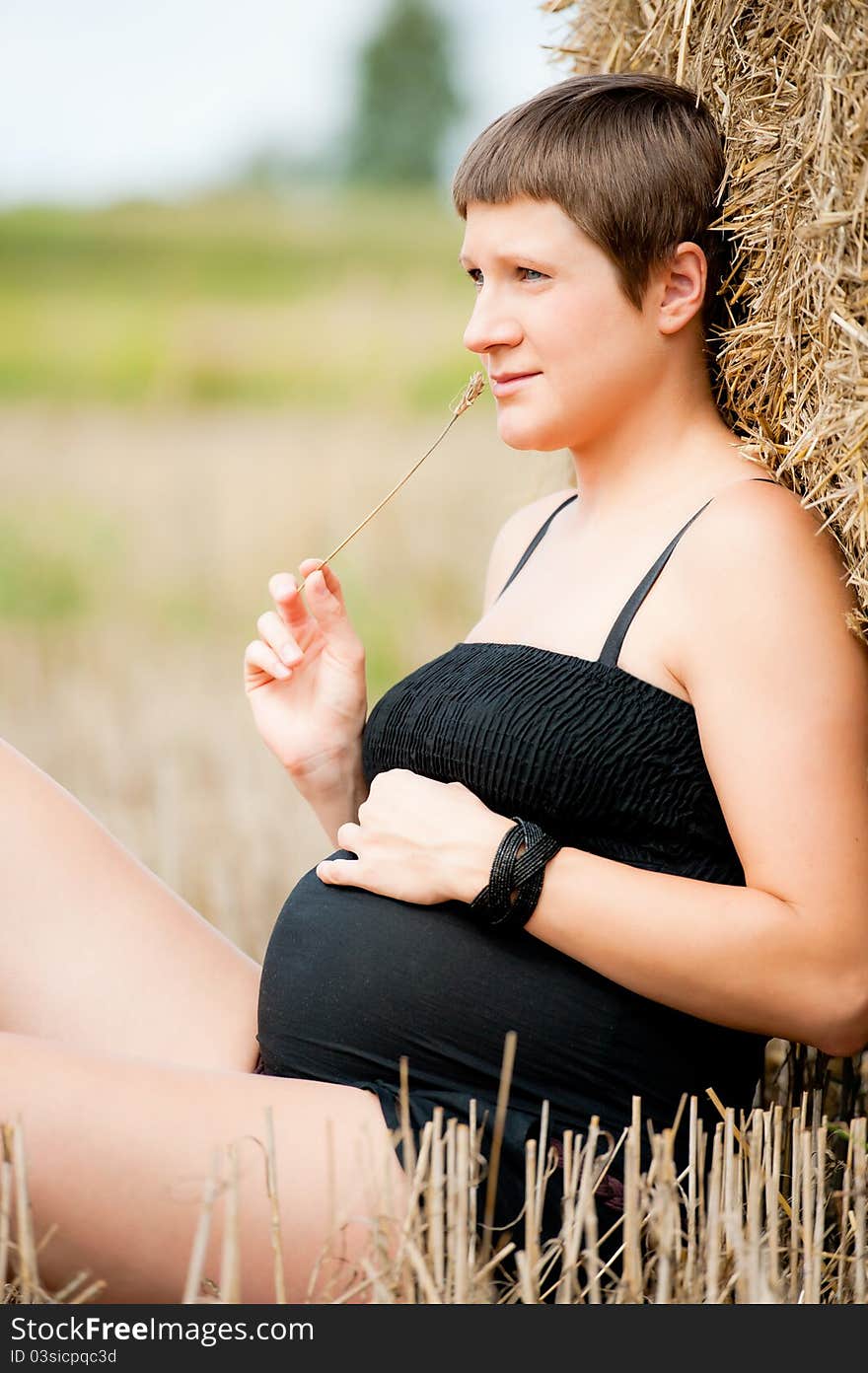 Pregnant woman on the field with straw