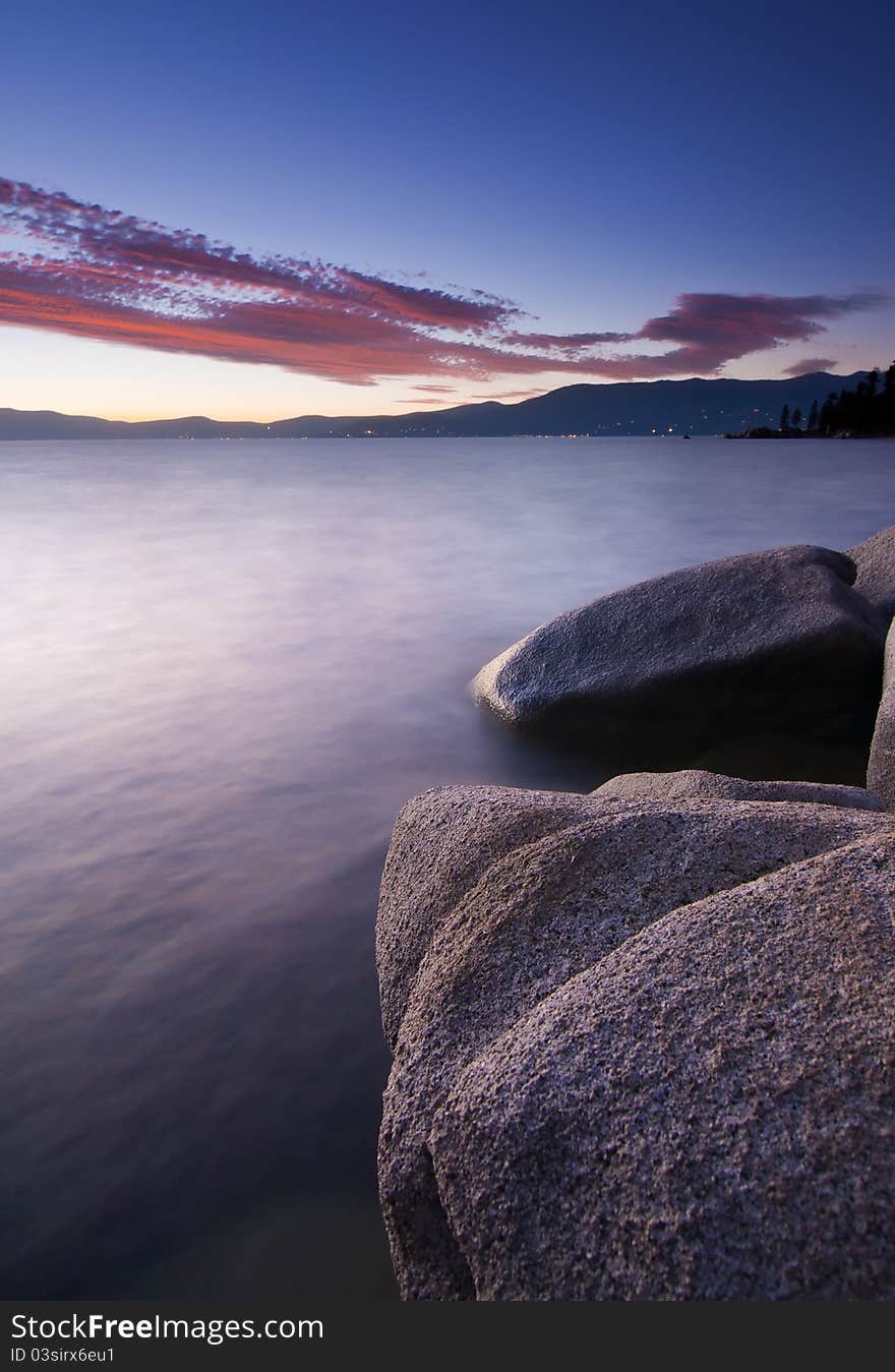 Smooth long exposure water with granite rocks and shoreline at sunset. Smooth long exposure water with granite rocks and shoreline at sunset