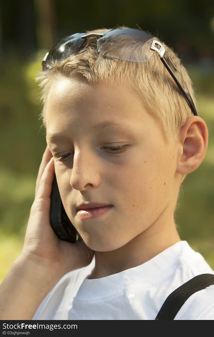 The boy the teenager in a white vest talks by a mobile phone. The boy the teenager in a white vest talks by a mobile phone