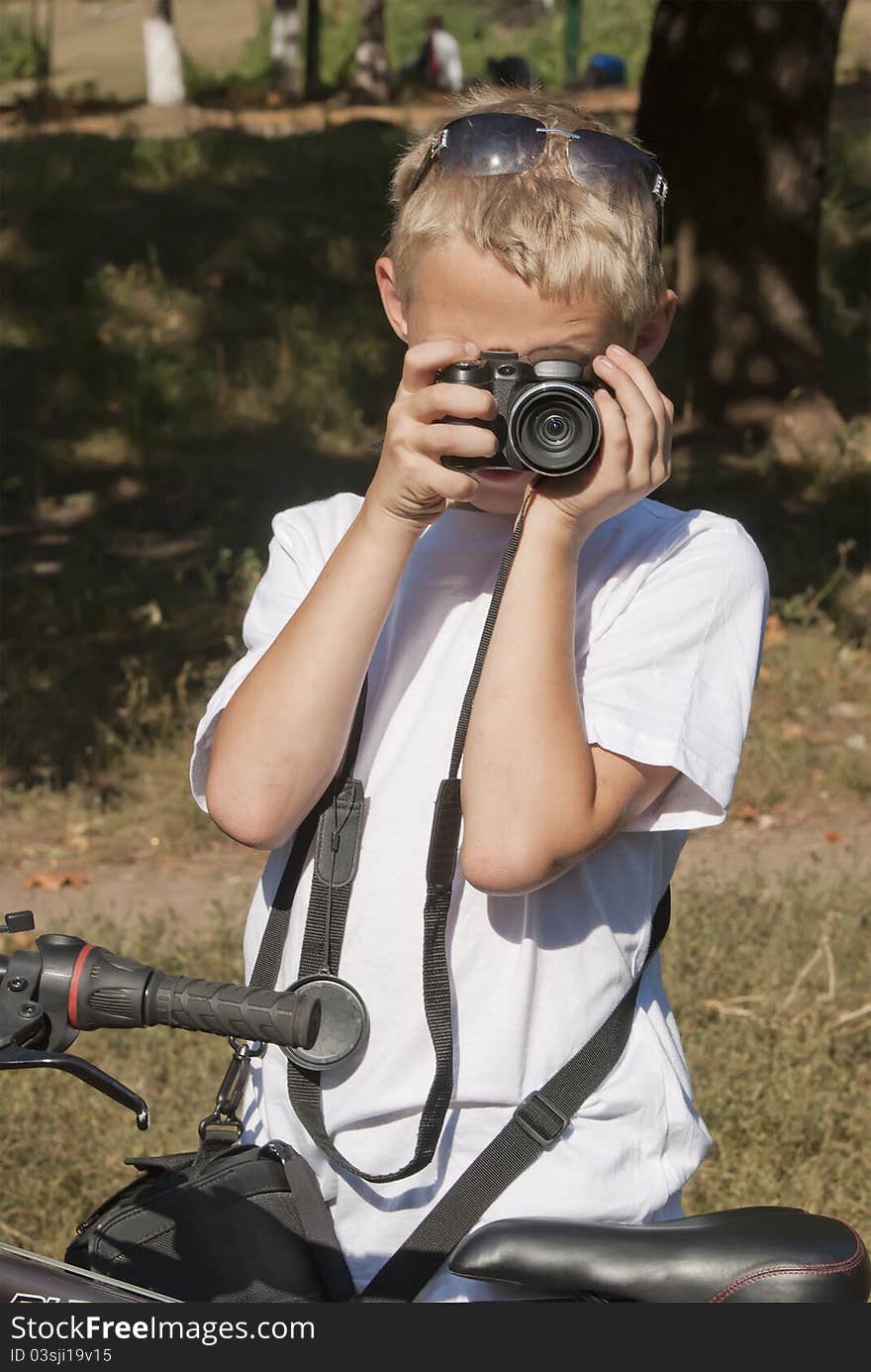 The boy in a white vest costs with the camera. The boy in a white vest costs with the camera