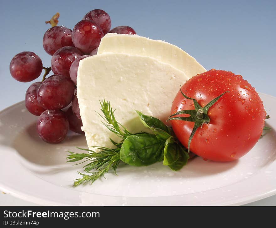 Mozarella cheese with tomato and grapes on white plate. Mozarella cheese with tomato and grapes on white plate