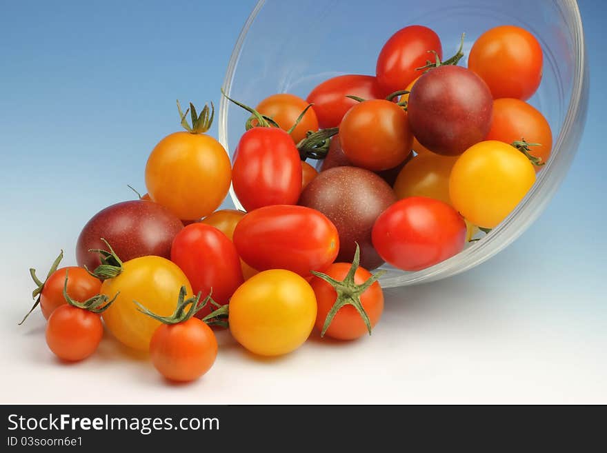 A variety of Cherry tomatoes spill out of a glass bowl.