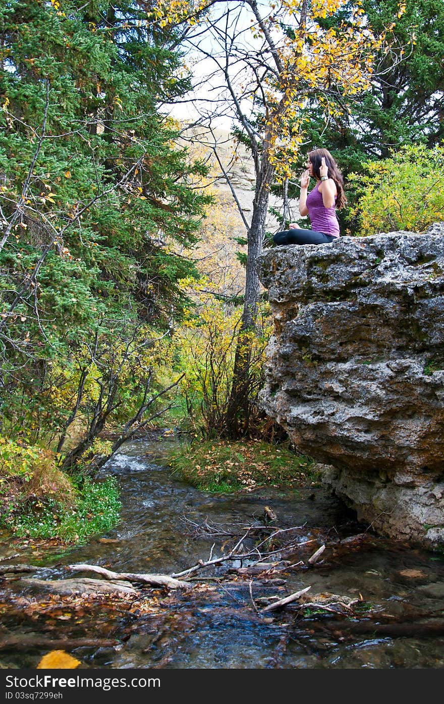 Young attractive girl sitting on the edge of a rock in autumn doing yoga and meditating with a creek running beneath her. Young attractive girl sitting on the edge of a rock in autumn doing yoga and meditating with a creek running beneath her