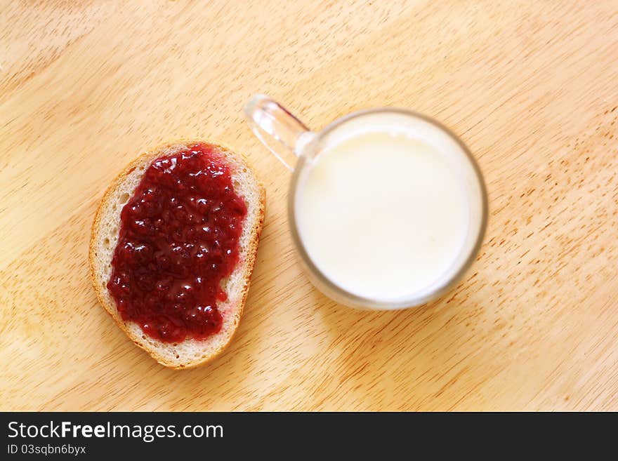 Bread with jam and glass of milk on wooden table