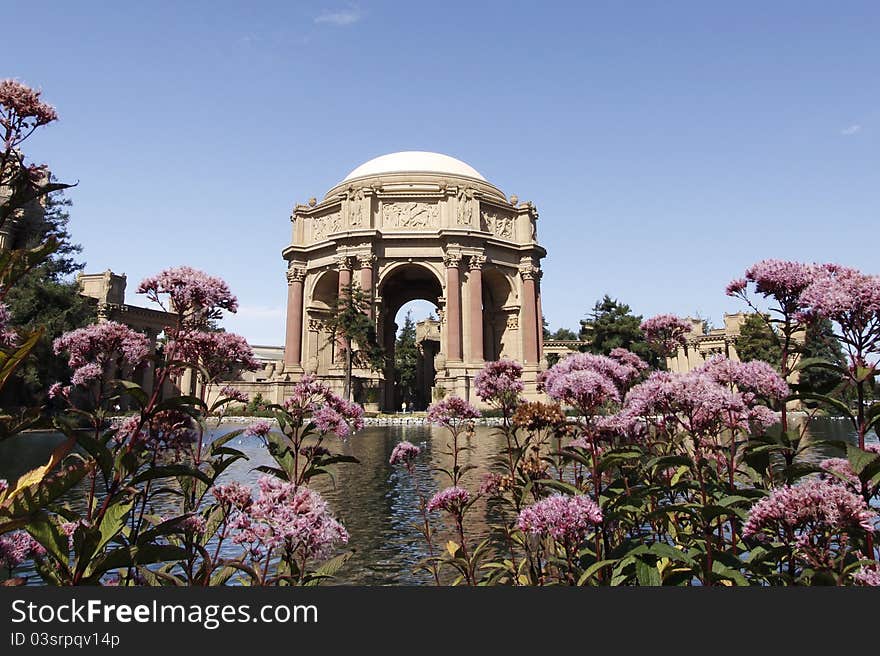 Palace of Fine Arts in San Francisco,California, view across pond, foreground framed by pink flowers.