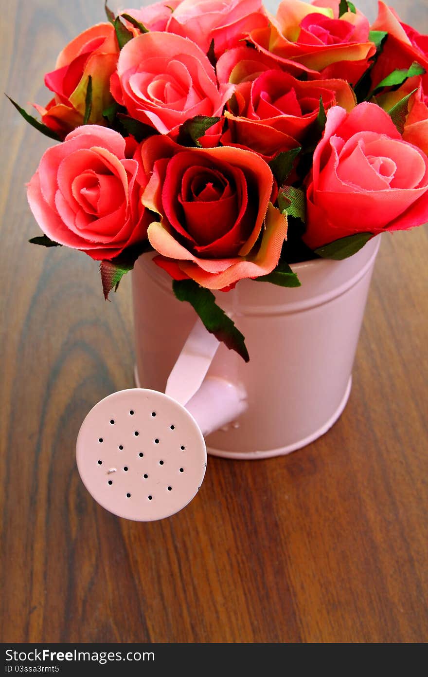 Plastic bouquet roses in watering can on wood background