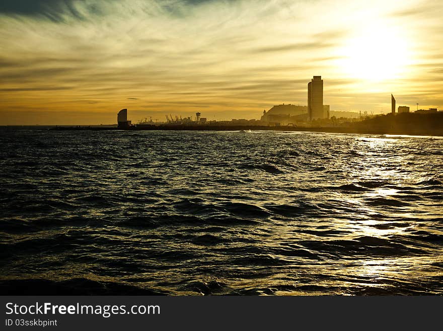 Bright yellow sundown seascape with silhouettes of Barcelona’s high-rise buildings and harbor cranes on the background. Bright yellow sundown seascape with silhouettes of Barcelona’s high-rise buildings and harbor cranes on the background