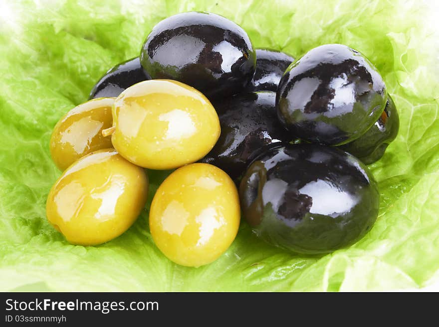 Black ripe olives in oil with a fresh green leaflet of salad