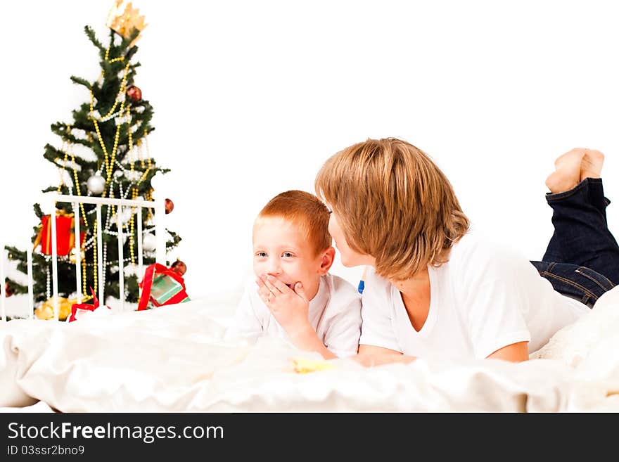 Mother with a son near a new-year tree on a white bed