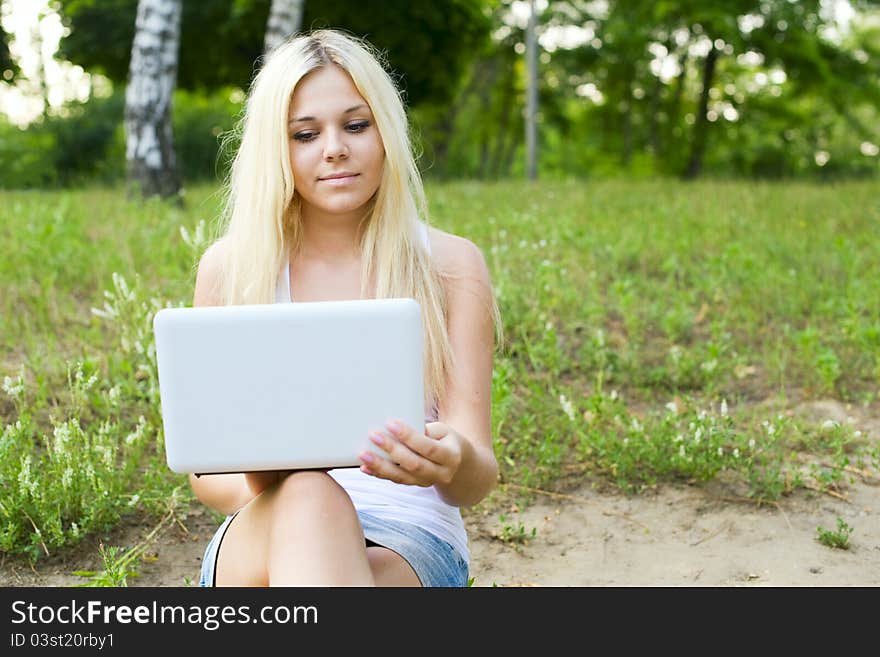 Portrait of a cheerful young woman sitting on lawn with a laptop. Portrait of a cheerful young woman sitting on lawn with a laptop