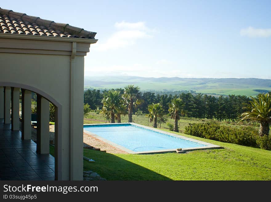 View across the verandah of a summer villa onto the blue sparkling swimming pool and mountain landscape in the distance. View across the verandah of a summer villa onto the blue sparkling swimming pool and mountain landscape in the distance