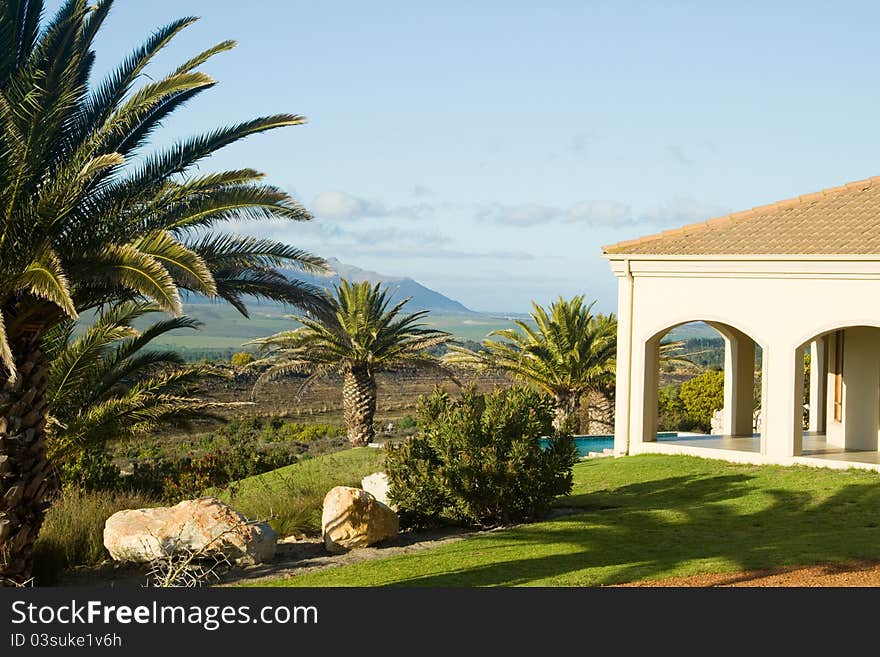 View past the verandah of a summer villa onto the blue sparkling swimming pool and mountain landscape in the distance. View past the verandah of a summer villa onto the blue sparkling swimming pool and mountain landscape in the distance