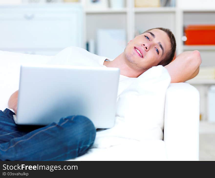 Handsome young man using laptop and lying on the sofa