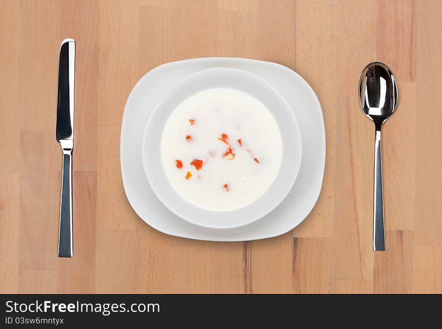 A plate of milk soup with vegetables on a wooden table with spoon and knife.