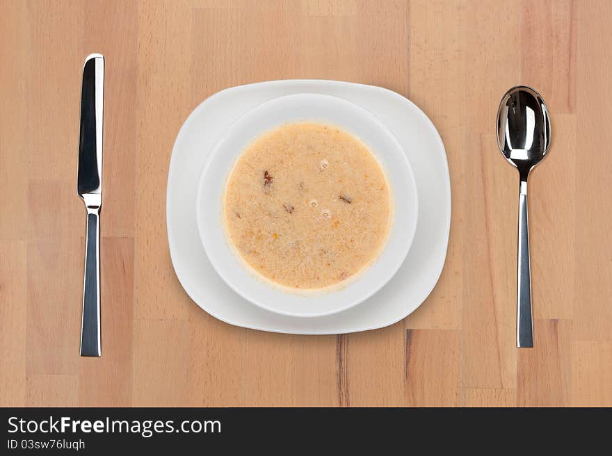 A plate of soup with a spoon and knife on a wooden table. A plate of soup with a spoon and knife on a wooden table.