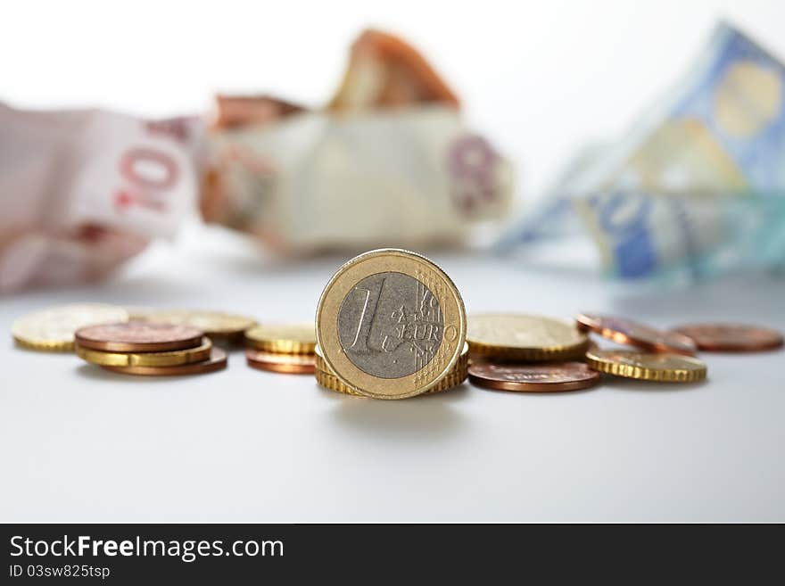 One euro coin standing alone with background of other coins and bank notes