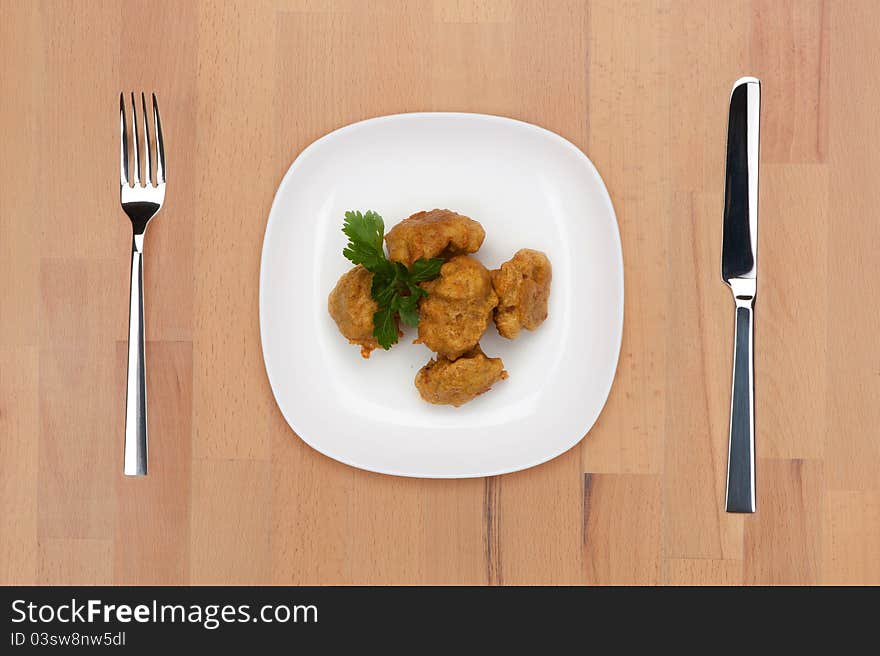 A plate of cooked battered cauliflower on a wooden table with fork and knife.