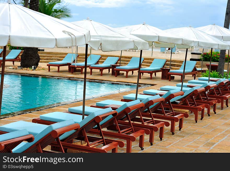 Wooden lounge chairs in row around swimming pool