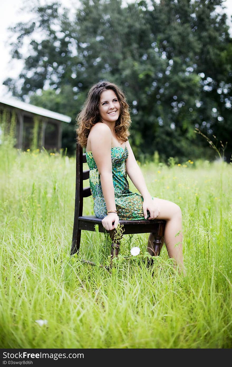 A smiling beautiful girl sitting on a chair in a field. A smiling beautiful girl sitting on a chair in a field.