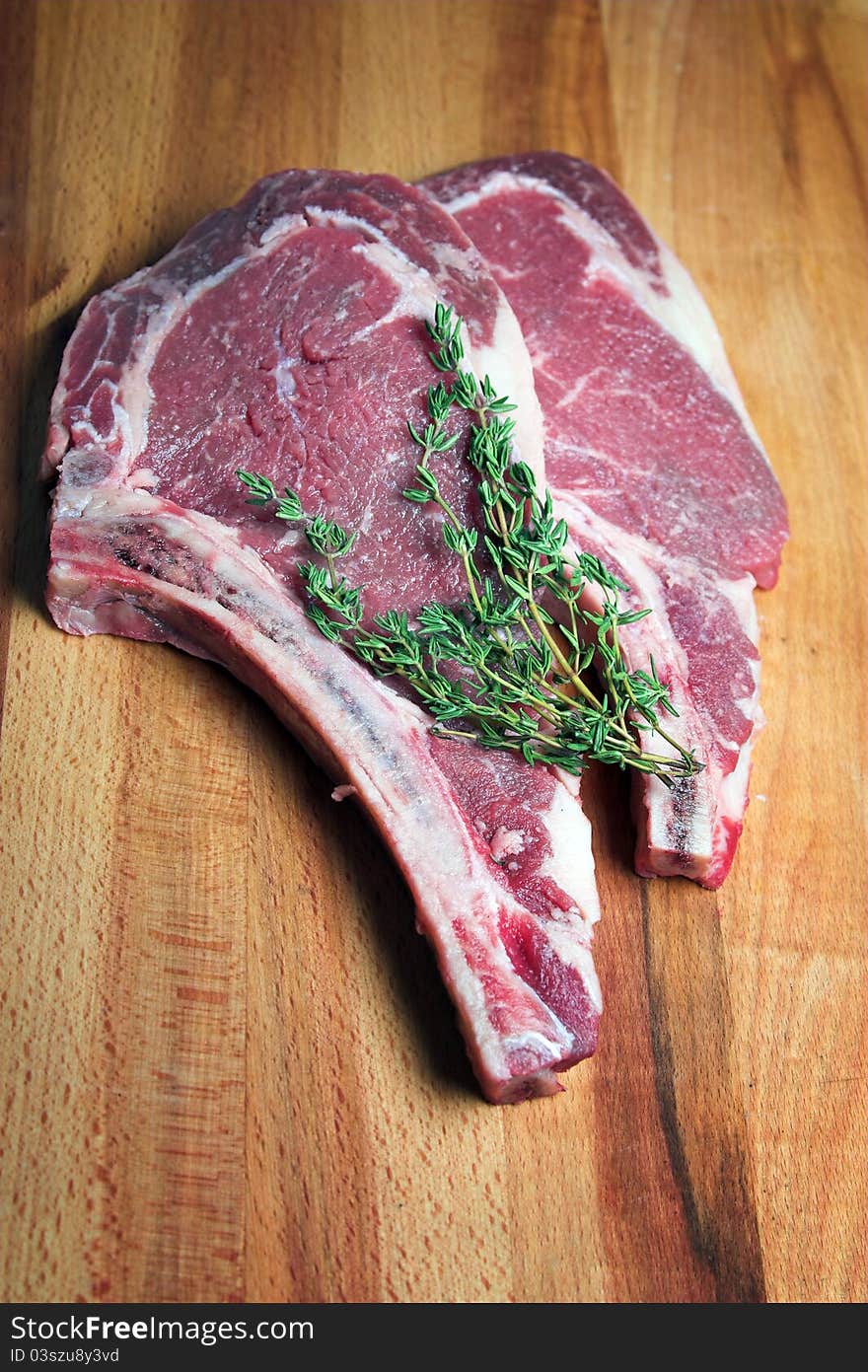 Two steaks raw with a sprig of thyme. Two steaks raw with a sprig of thyme