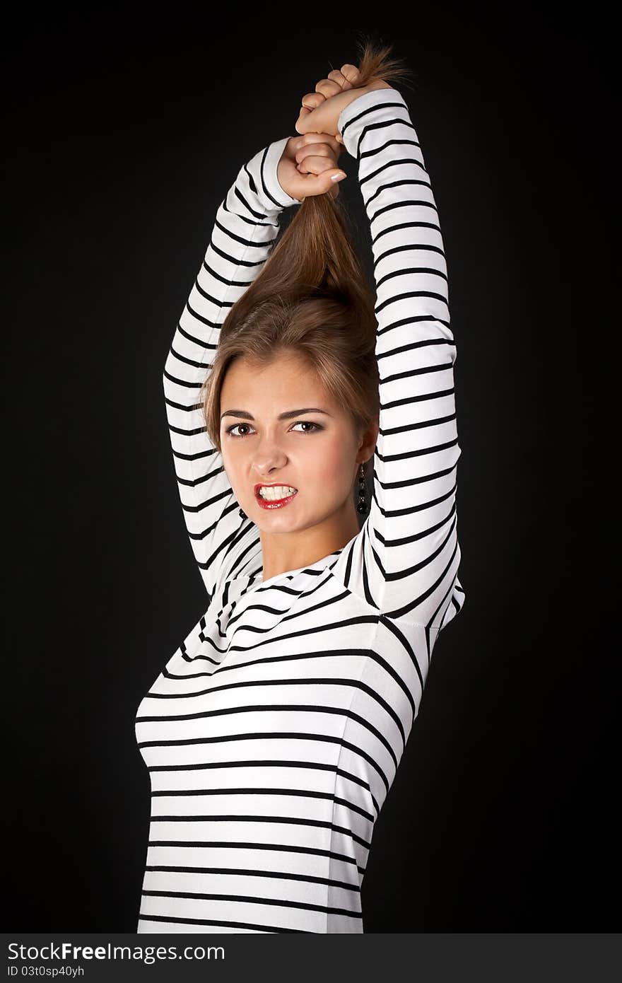 Beautiful girl in a striped dress pulls his hair on a black background