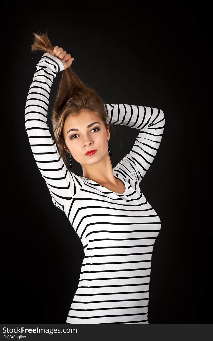 Beautiful girl in a striped dress pulls his hair on a black background