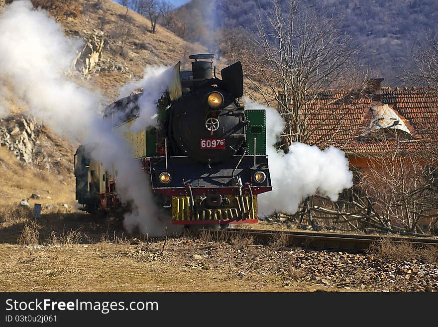 Steam train from late nineteenth century in sunny winter next to country home. Green and red retro locomotive.