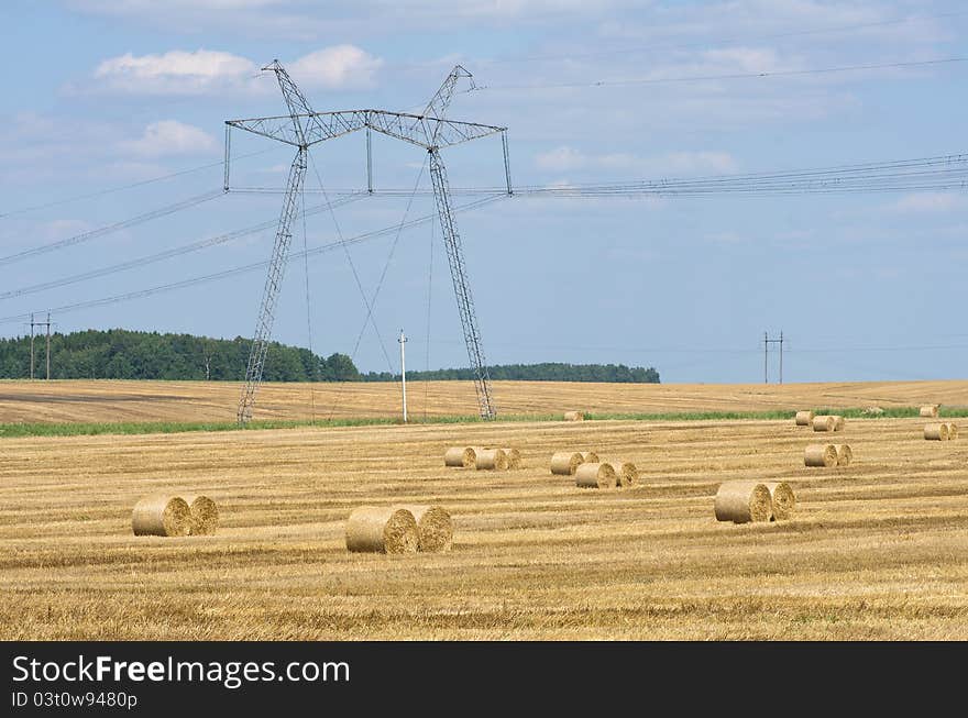 The high-voltage line running through a field with rolls of straw. The high-voltage line running through a field with rolls of straw