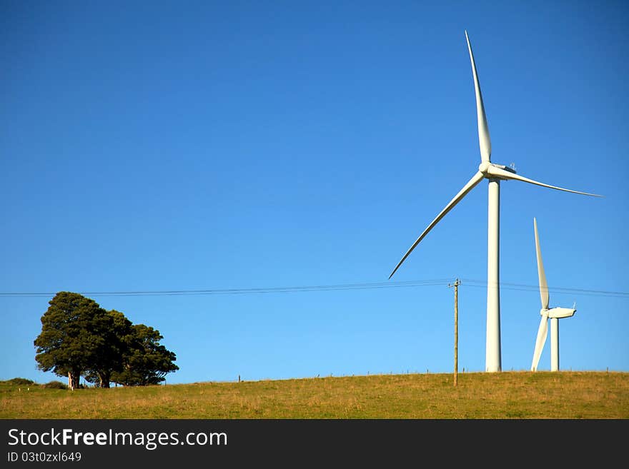 Two wind turbines in a paddock set against a blue sky