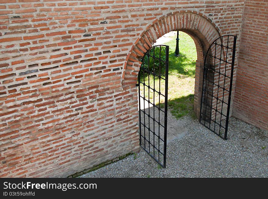 Opened iron forged gate with brick wall