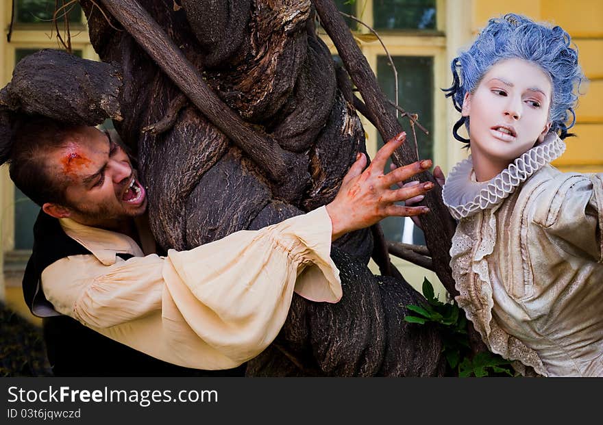 Couple in medieval costumes - male vampire reching hand to women with blue wig. Couple in medieval costumes - male vampire reching hand to women with blue wig