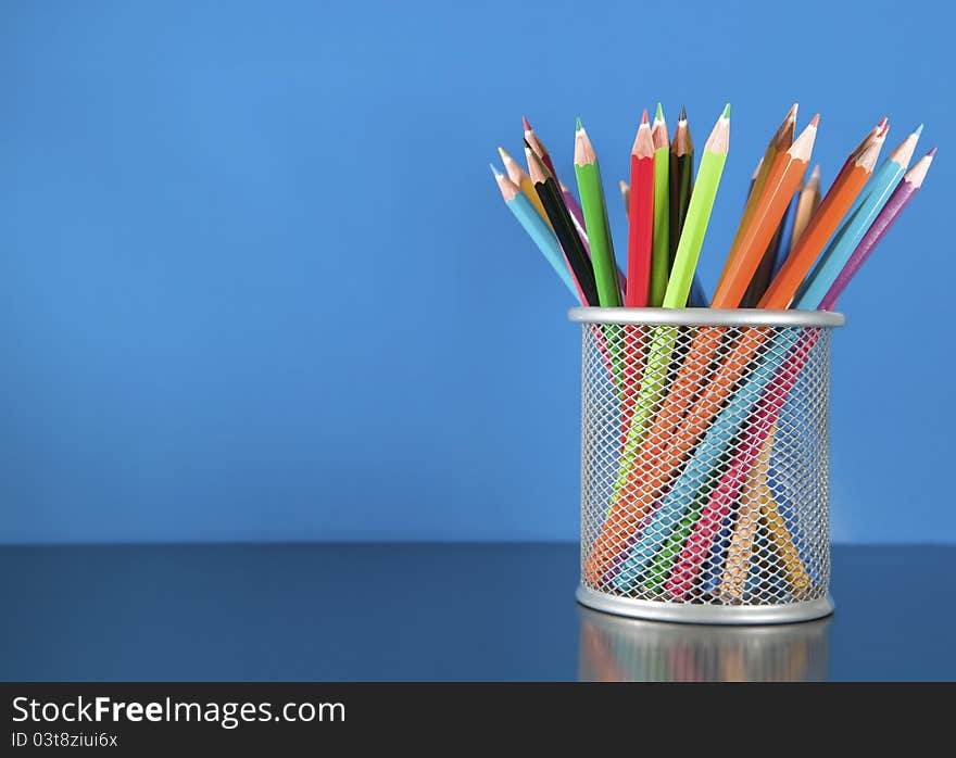 Colour pencils in the basket on the blue background