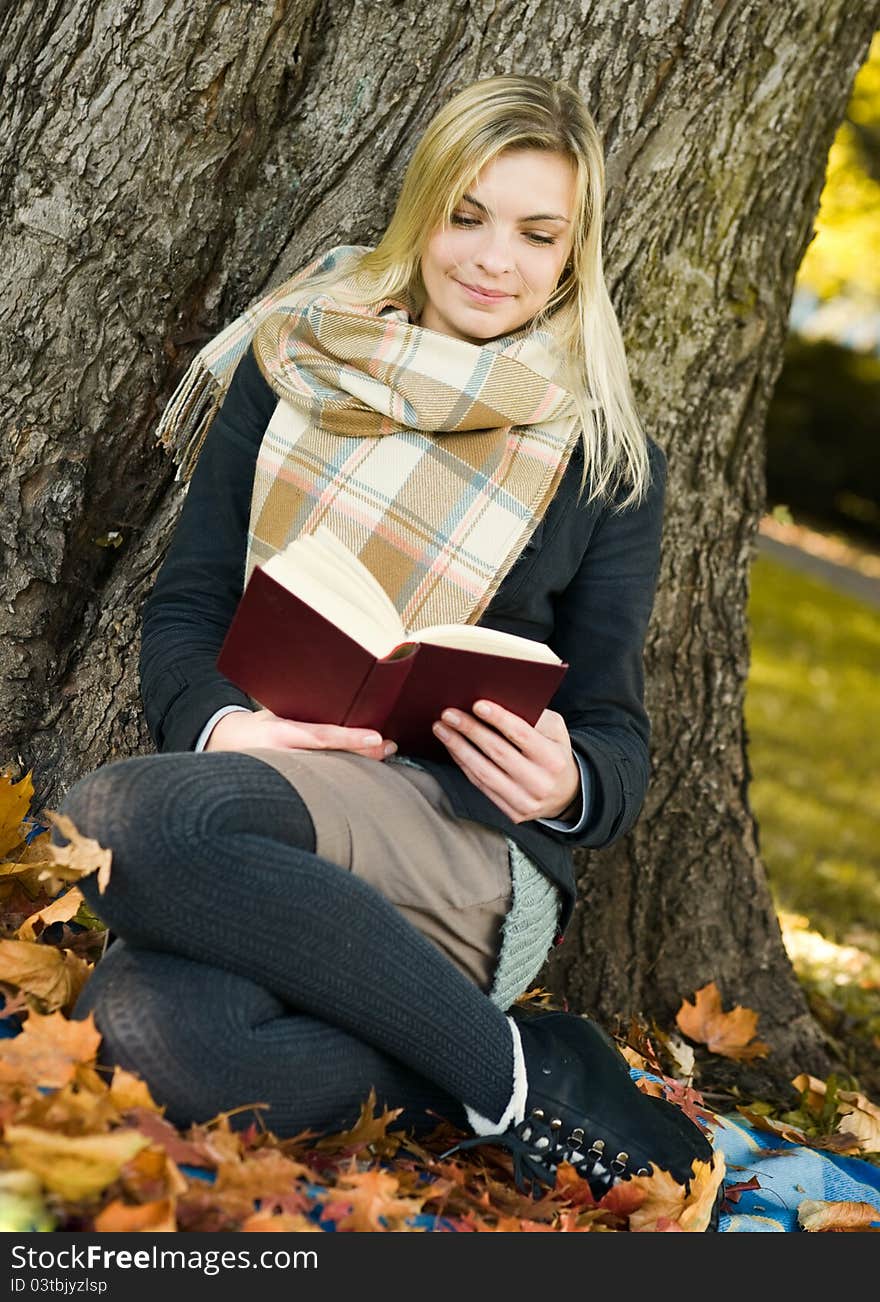 Young beautiful woman reading the book in at autumn park. Young beautiful woman reading the book in at autumn park