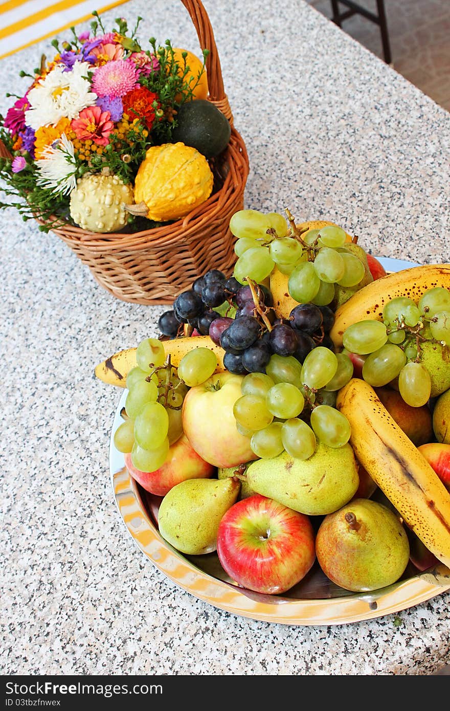 Flower basket and fruit plateau on grey outdoor table.