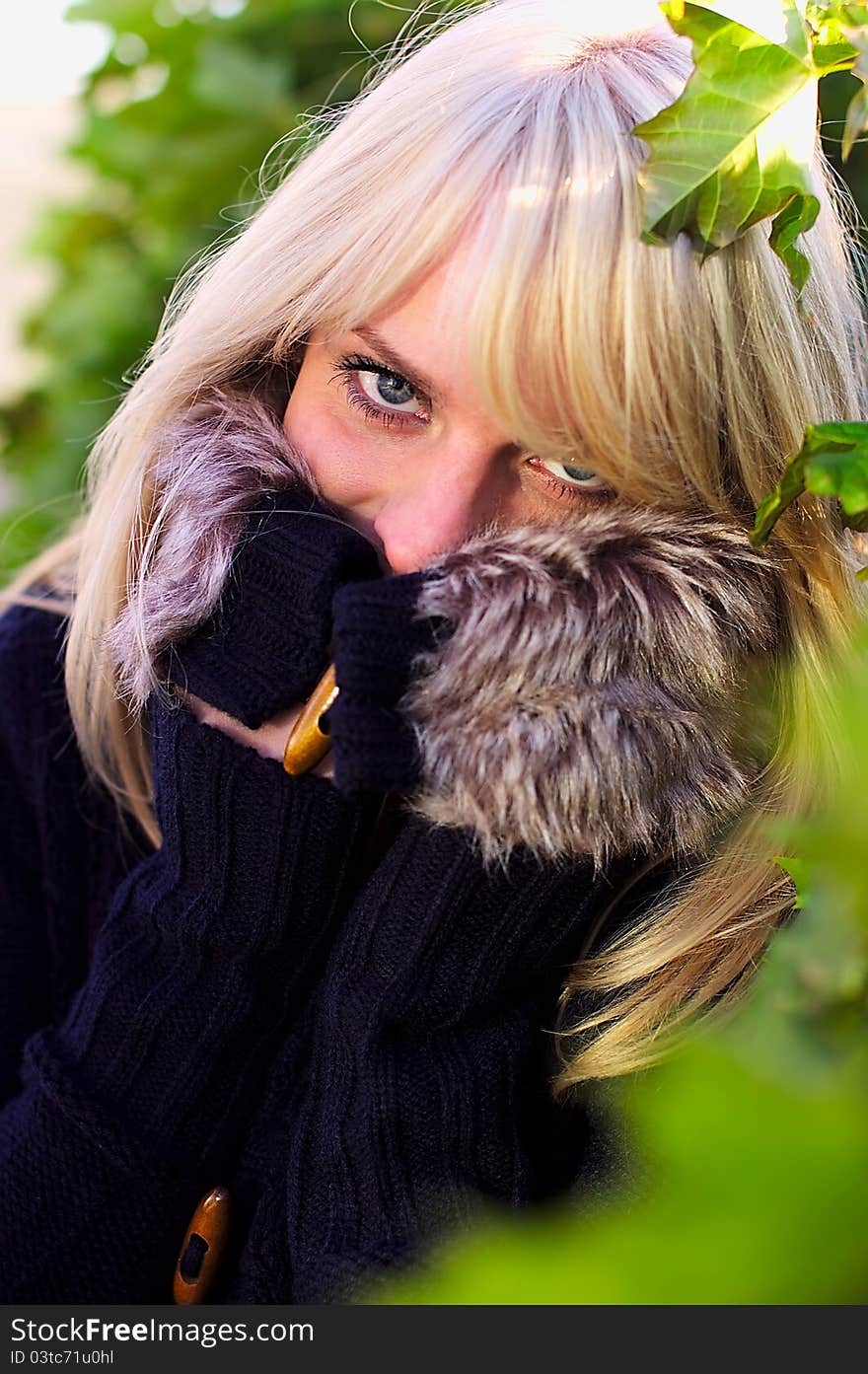 Blond girl hides in her sweater, the frame around her of natural green leaves. Blond girl hides in her sweater, the frame around her of natural green leaves