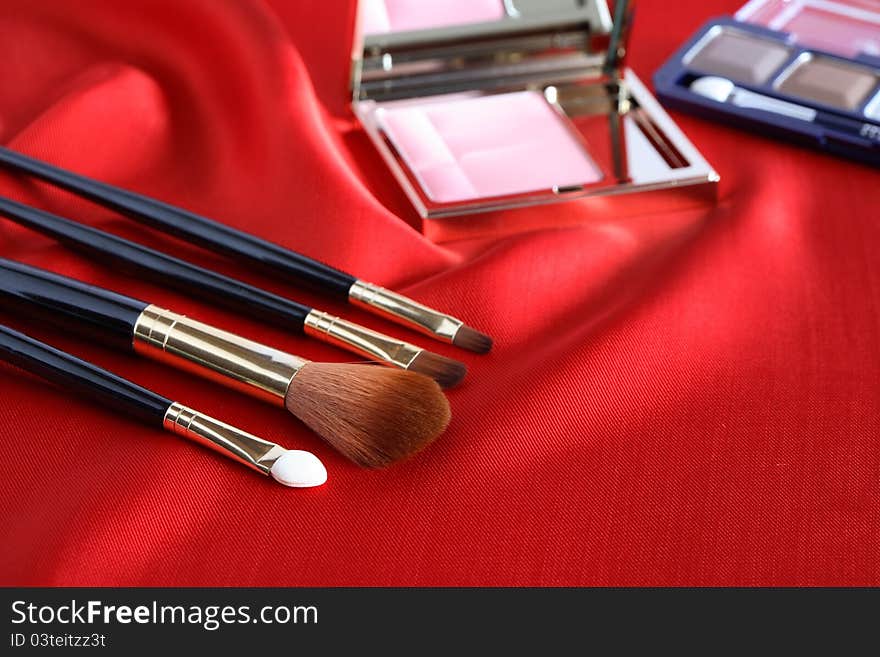 Few makeup brushes and rouge on red silk surface. Few makeup brushes and rouge on red silk surface