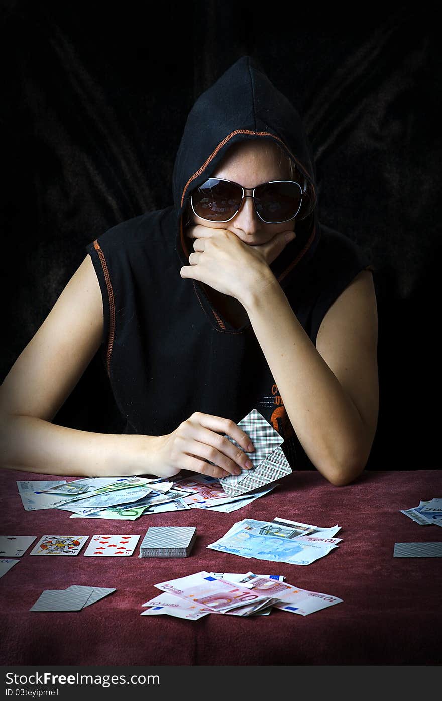 Poker face. Person in sun glasses and hood playing poker at the table with cards and money. Poker face. Person in sun glasses and hood playing poker at the table with cards and money