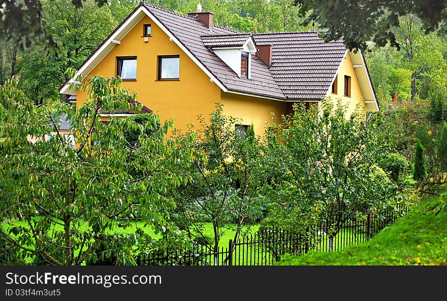 Yellow rural house hidden in green garden