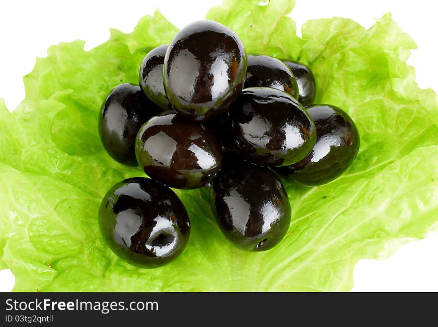 Black ripe olives in oil with a fresh green leaflet of salad