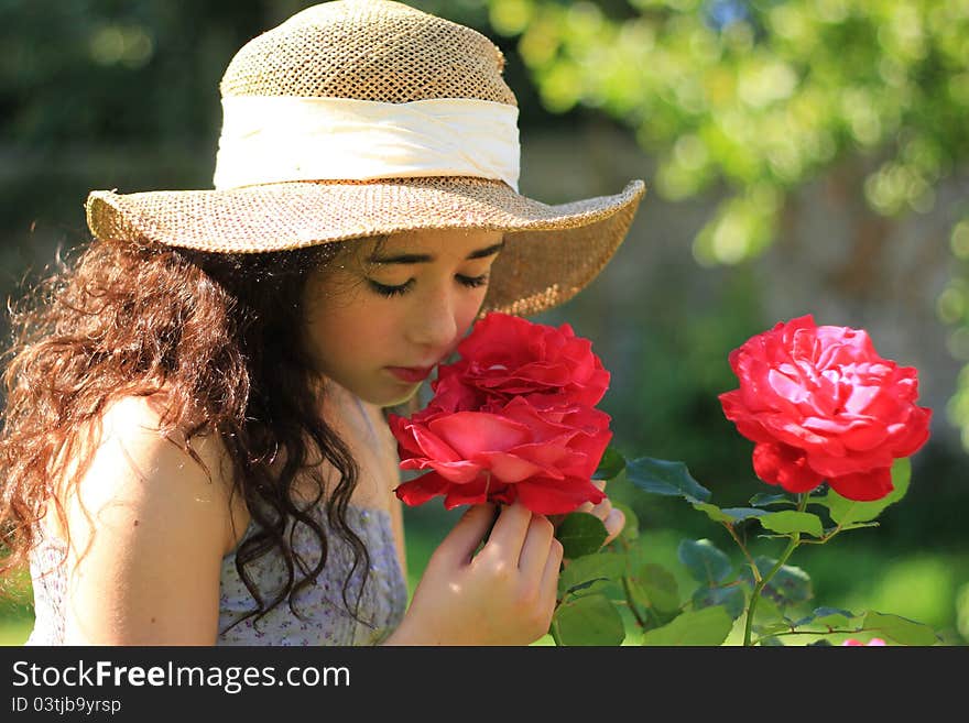 Pretty girl in straw hat smelling red roses in a garden. Pretty girl in straw hat smelling red roses in a garden