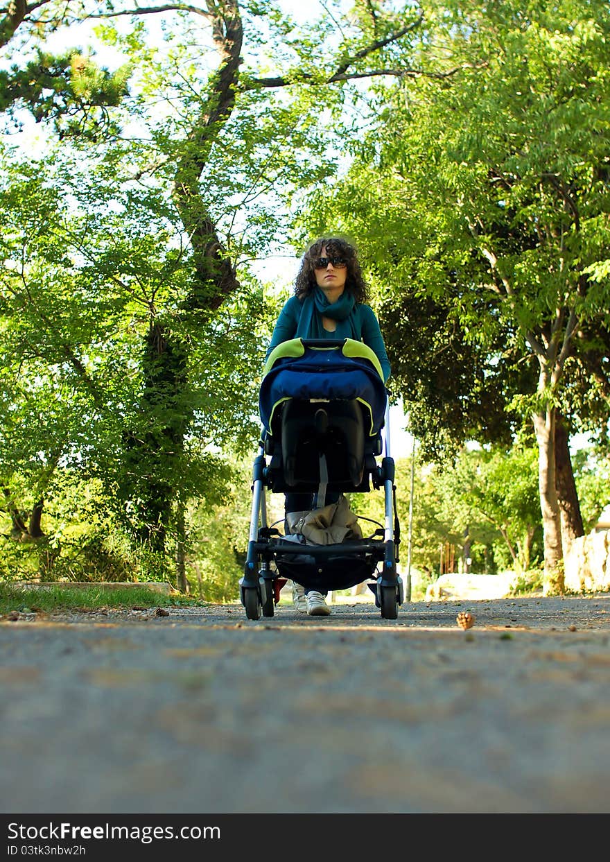Mother walking with her child in nature, pushing children carts in the park on nice weather in stroller. Mother walking with her child in nature, pushing children carts in the park on nice weather in stroller