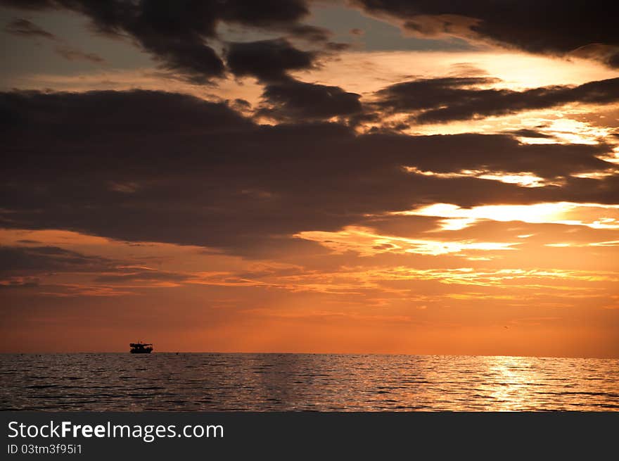 Dramatic orange sunset with clouds and boat on sea