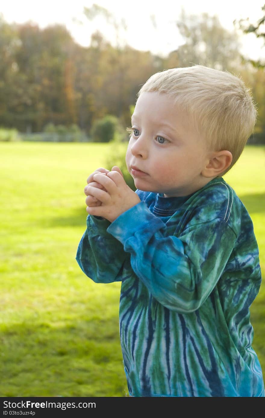 A little boy with a blue tie dyed shirt stands with his hands clasped, seemingly in prayer. A little boy with a blue tie dyed shirt stands with his hands clasped, seemingly in prayer